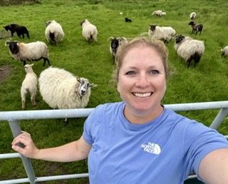 A retreat guest smiling by a gate, with Achill sheep behind.